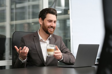 Photo of Man with cup of coffee working on laptop at black desk in office