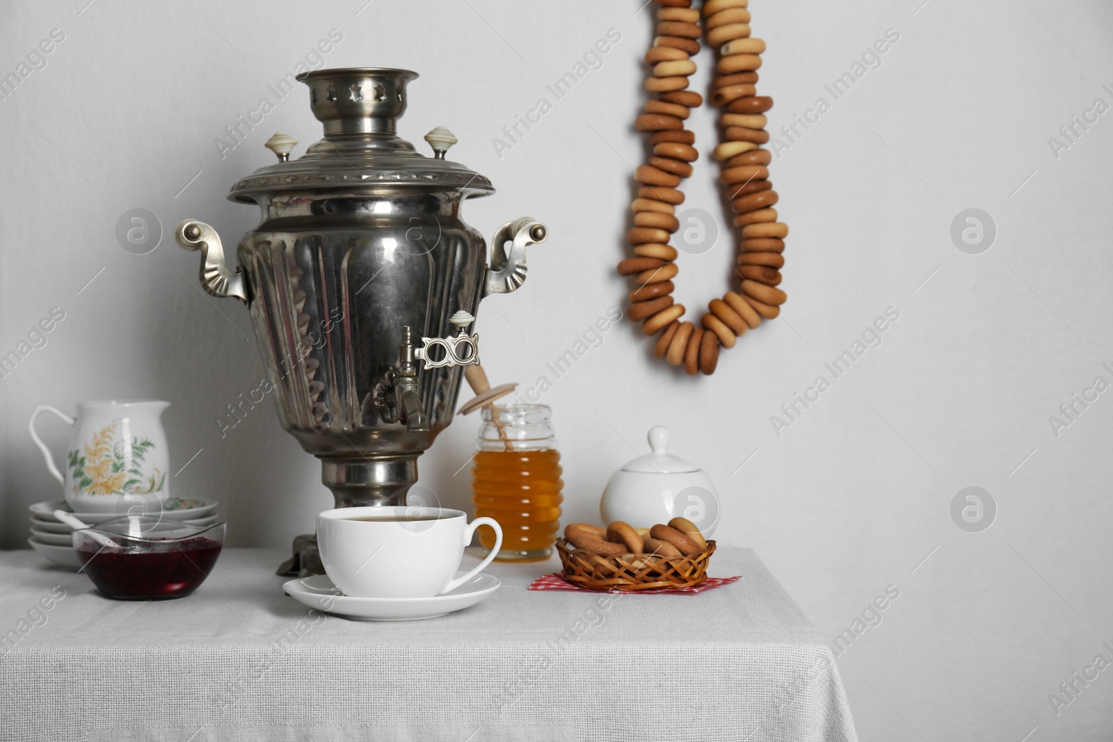 Photo of Composition with delicious ring shaped Sushki (dry bagels) and tea on white tablecloth near wall