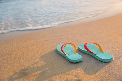 Bright turquoise beach slippers on sand near sea, space for text