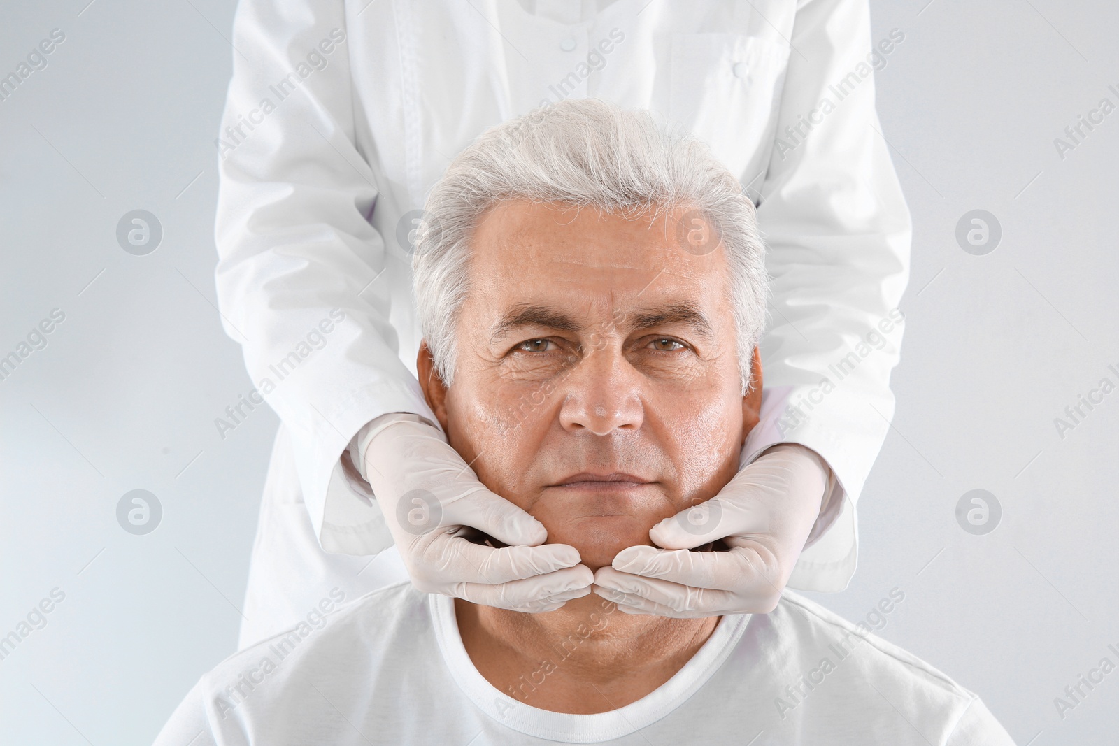 Photo of Doctor examining senior man face before cosmetic surgery on white background