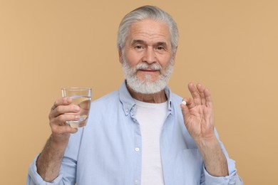 Photo of Senior man with glass of water and pill on beige background