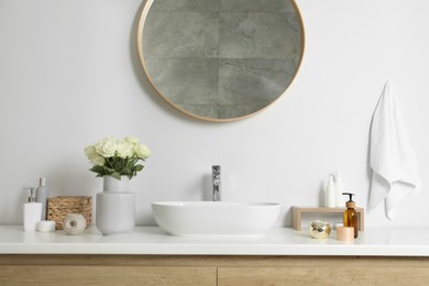 Photo of Vase with beautiful white roses and toiletries near sink in bathroom