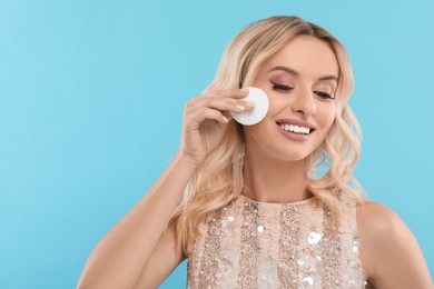 Smiling woman removing makeup with cotton pad on light blue background. Space for text