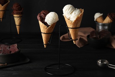 Ice cream scoops in wafer cones on black wooden table against dark background