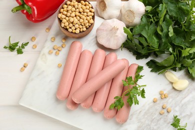 Photo of Fresh raw vegetarian sausages and vegetables on white wooden table, flat lay