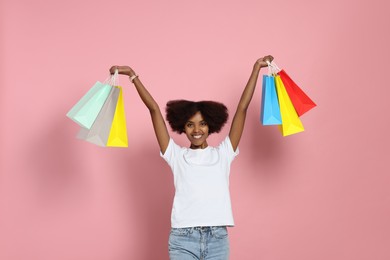 Photo of Happy African American woman with shopping bags on pink background