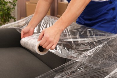 Photo of Worker wrapping sofa in stretch film indoors, closeup