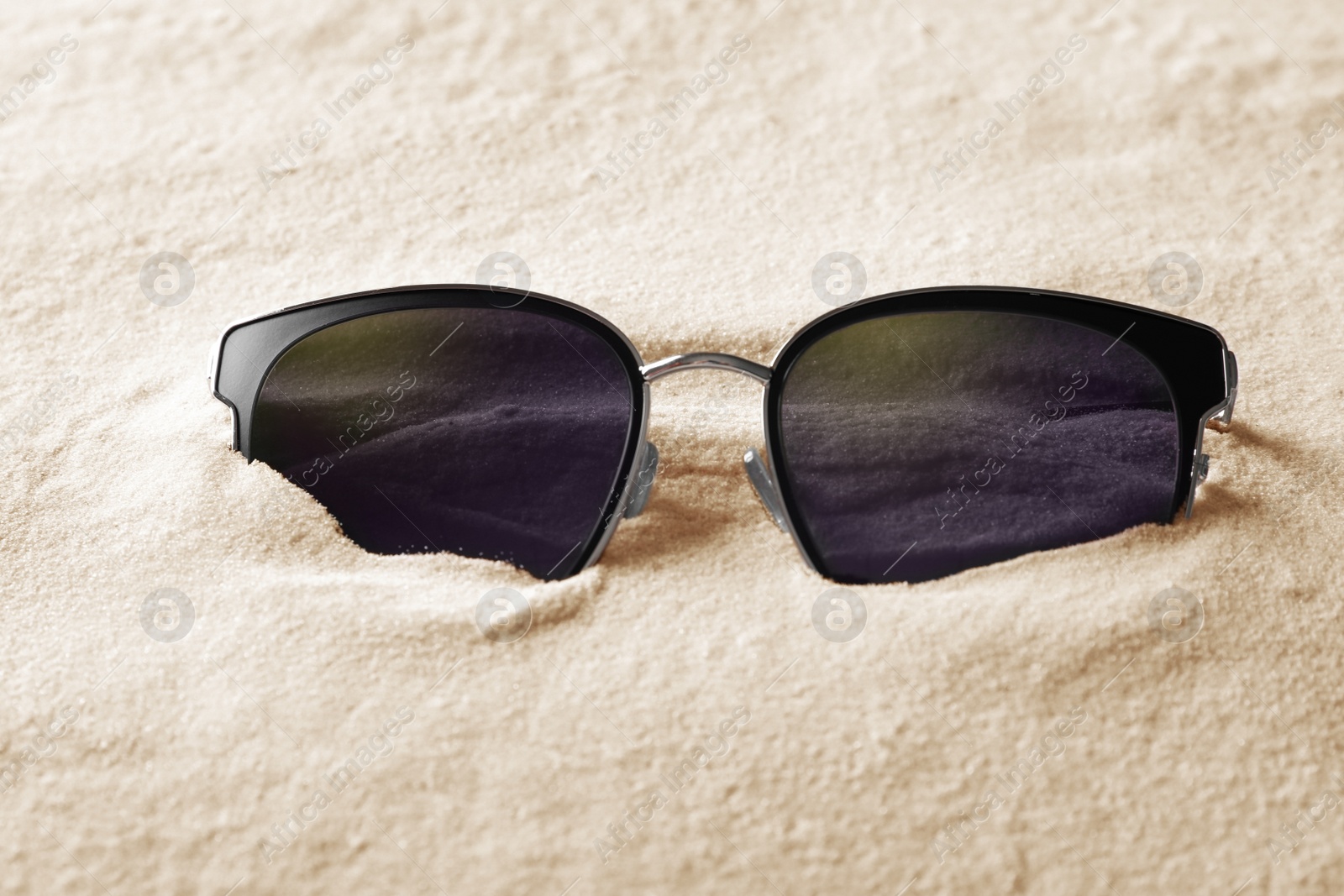 Photo of Stylish sunglasses on white sand. Fashionable accessory