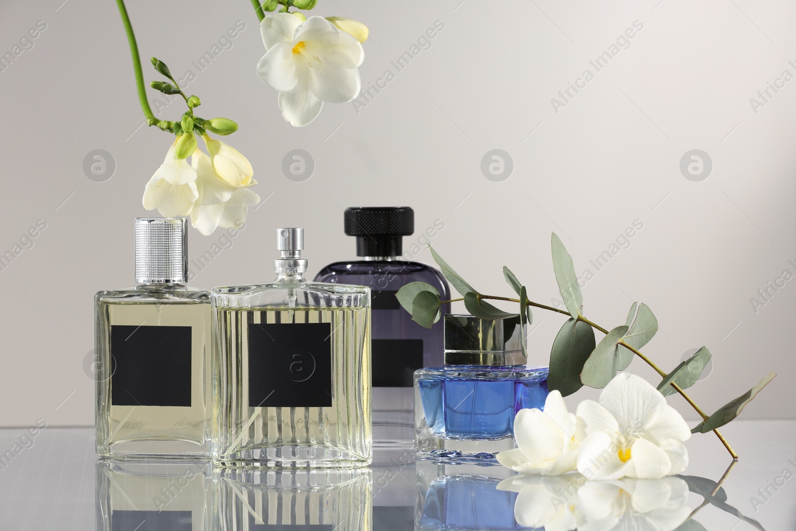 Photo of Luxury perfumes and floral decor on mirror surface against light grey background