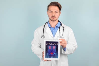 Photo of Male doctor holding tablet with urinary system on screen against color background