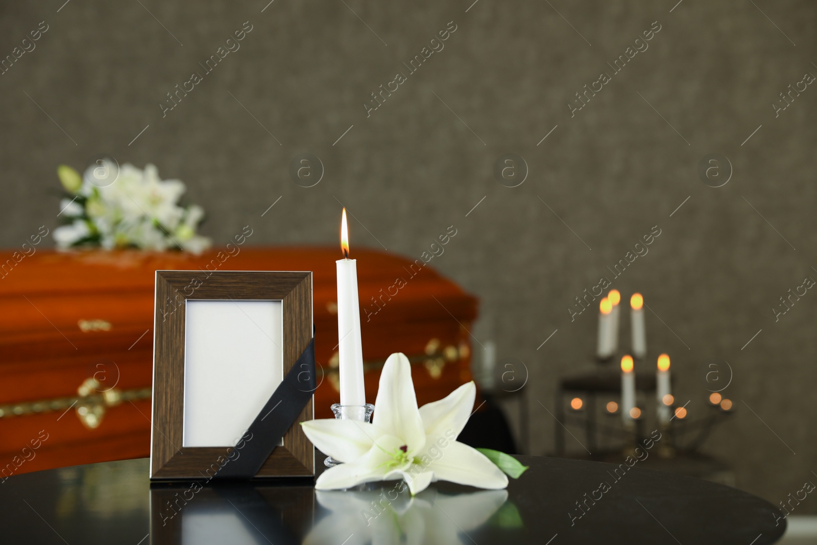 Photo of Black photo frame with burning candle and white lily on table in funeral home