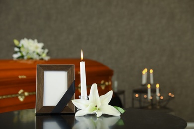 Photo of Black photo frame with burning candle and white lily on table in funeral home