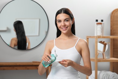 Young woman pouring micellar water onto cotton pad indoors