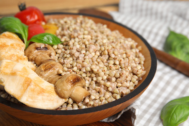 Photo of Tasty buckwheat porridge with meat and mushrooms in bowl, closeup