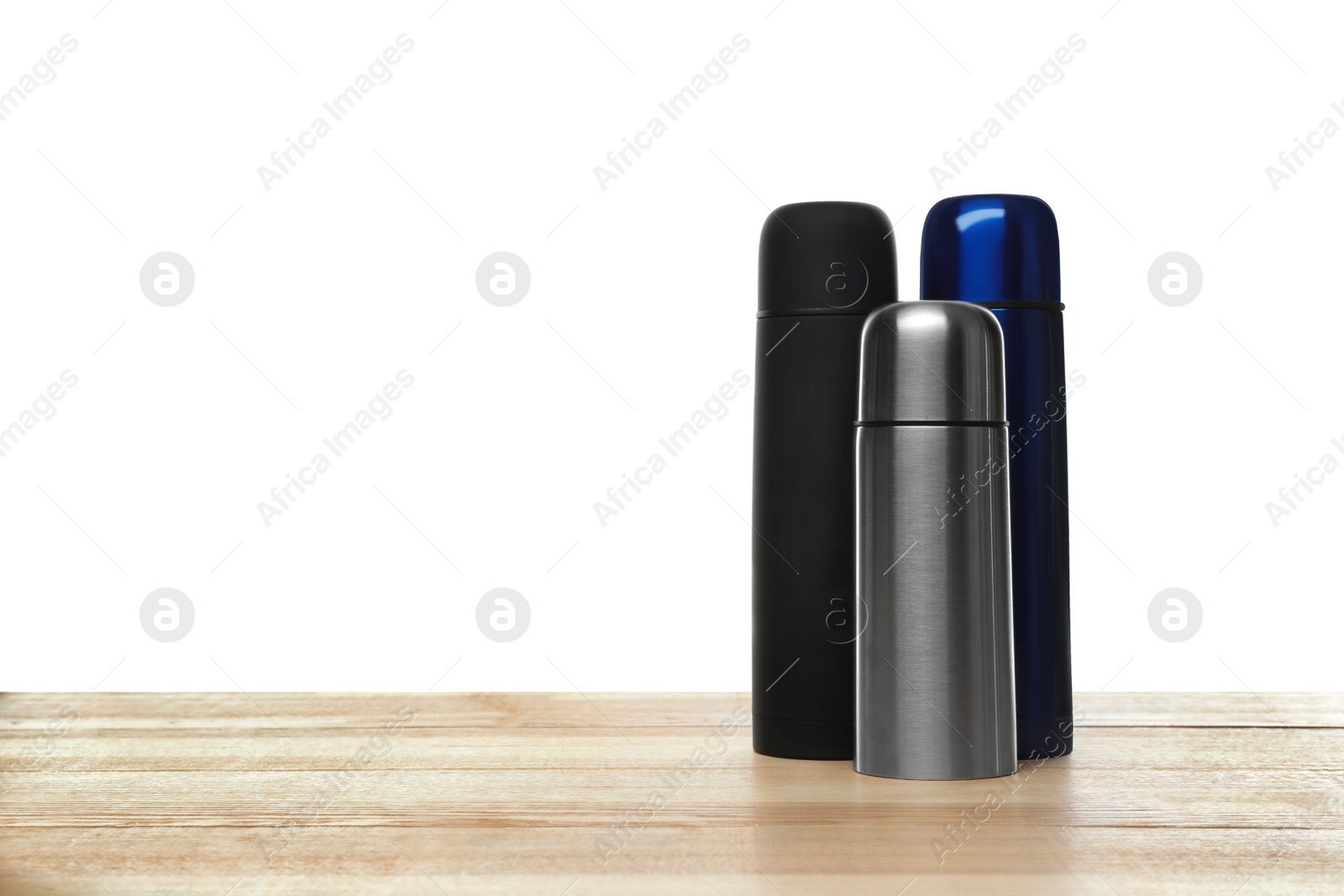 Photo of Stylish thermo bottles on wooden table against white background