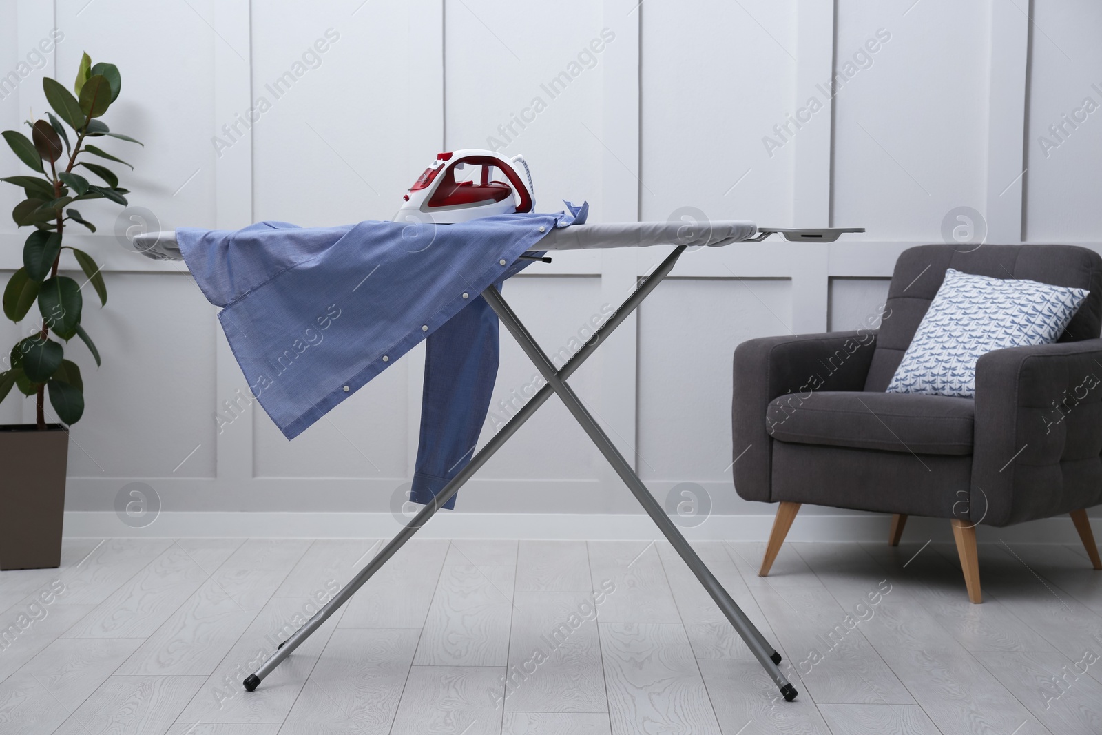 Photo of Modern iron and clean shirt on board in room