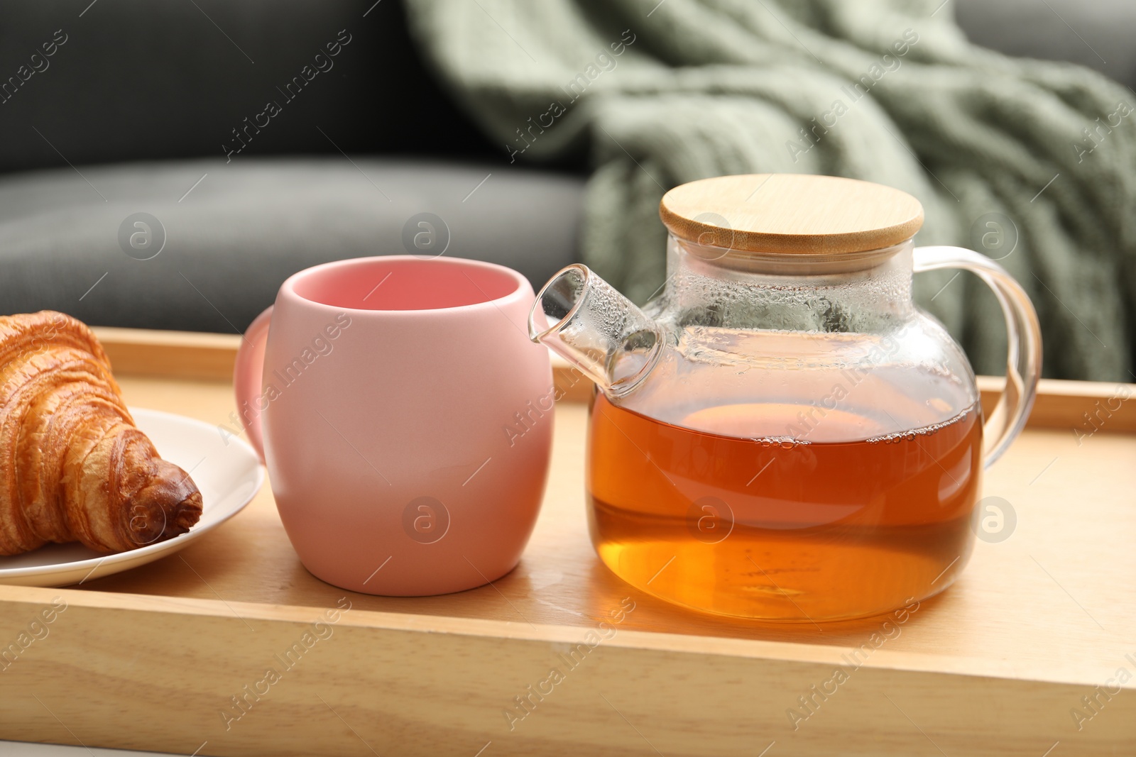 Photo of Aromatic tea in teapot, cup and tasty croissant on table indoors