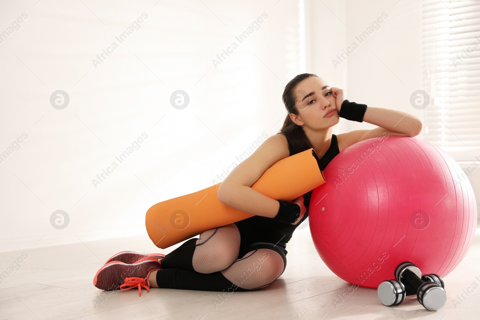 Photo of Lazy young woman with sport equipment indoors. Space for text