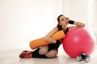 Photo of Lazy young woman with sport equipment indoors. Space for text
