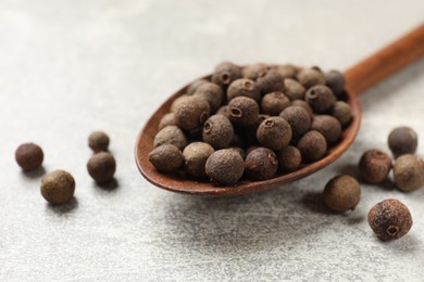 Photo of Aromatic allspice pepper grains in wooden spoon on grey table, closeup