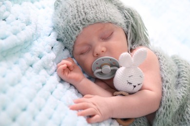 Cute newborn baby with pacifier sleeping on light blue blanket, closeup