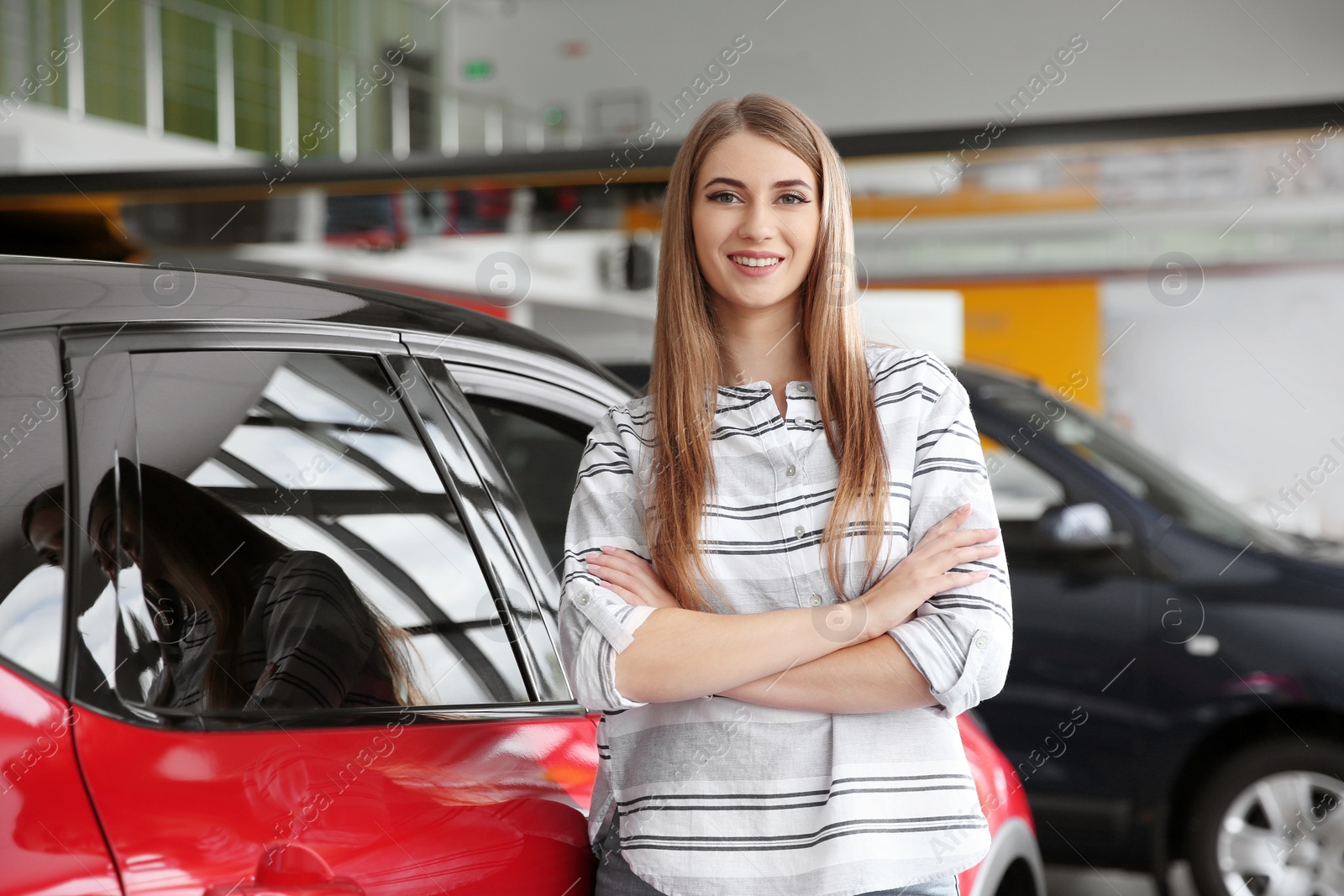 Photo of Young woman near new car in modern auto dealership