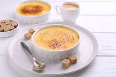 Delicious creme brulee in bowls, vanilla pods, sugar cubes and coffee on white wooden table