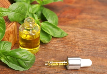 Photo of Glass bottle of oil with basil leaves and space for text on wooden table