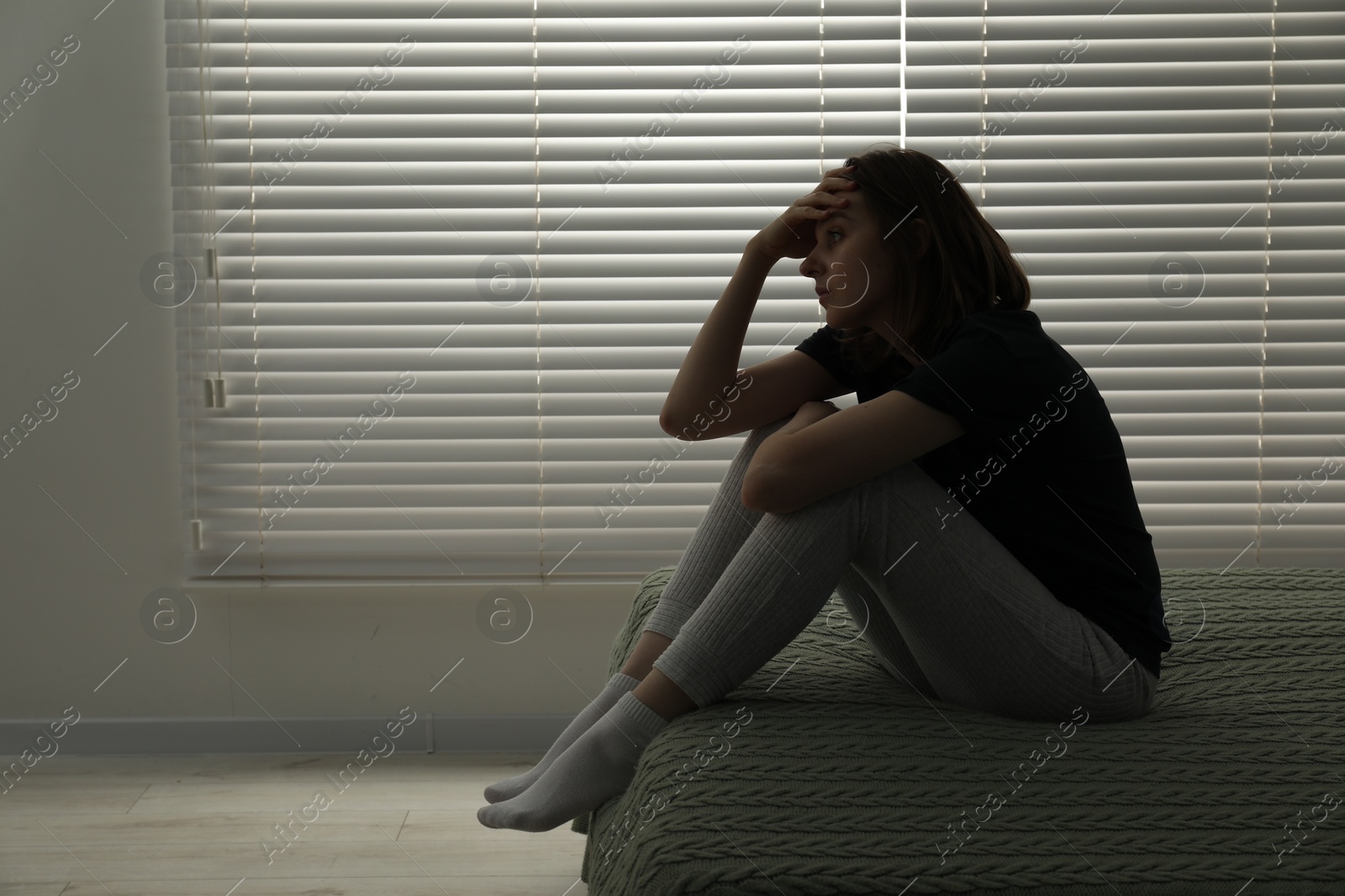 Photo of Sad young woman sitting on bed at home, space for text