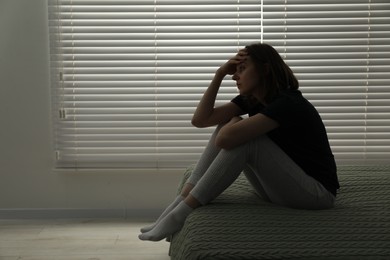 Photo of Sad young woman sitting on bed at home, space for text