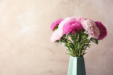 Beautiful aster flower bouquet in vase against color background. Space for text