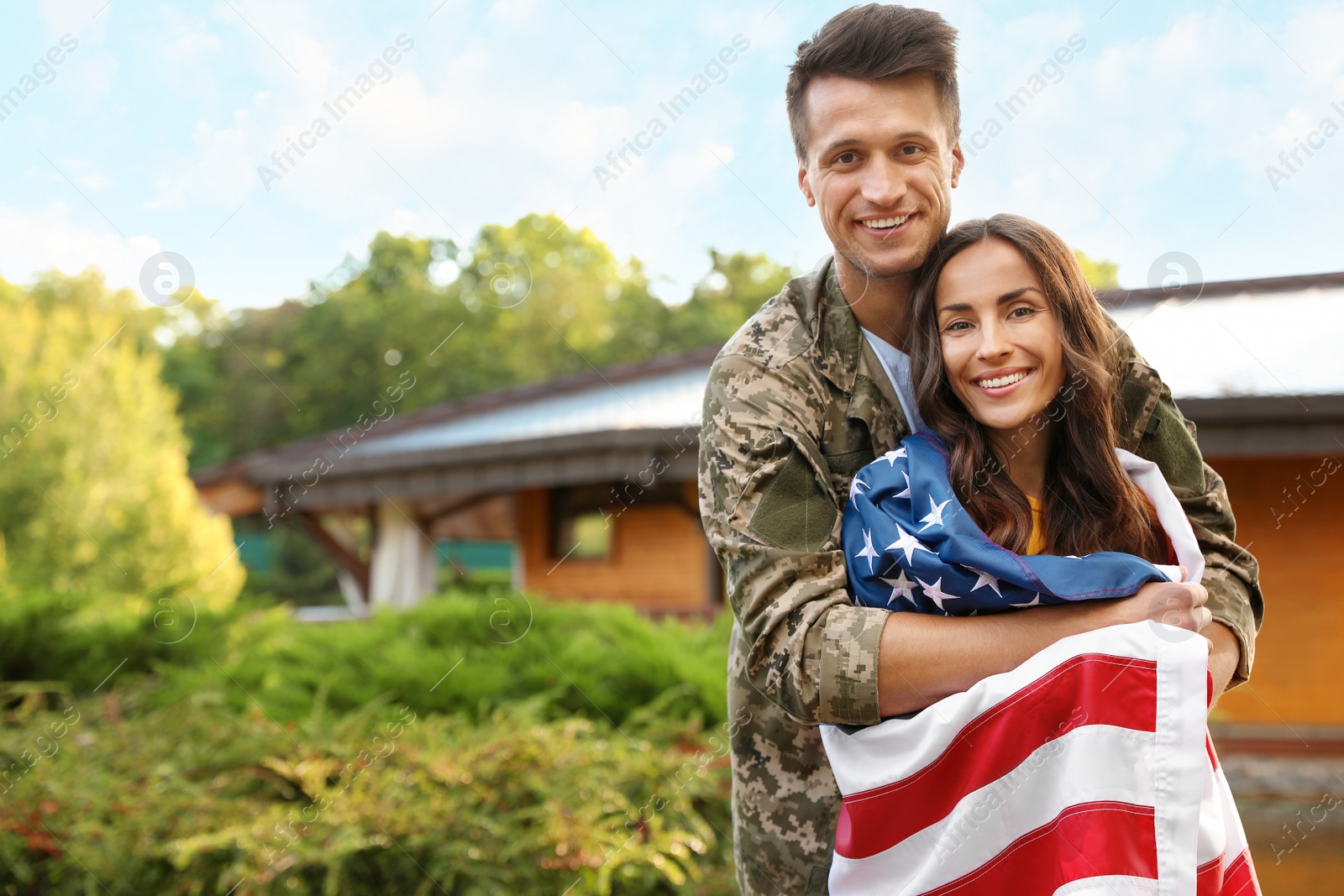 Photo of Man in military uniform with American flag and his wife outdoors