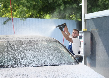 Young worker cleaning automobile with high pressure water jet at car wash