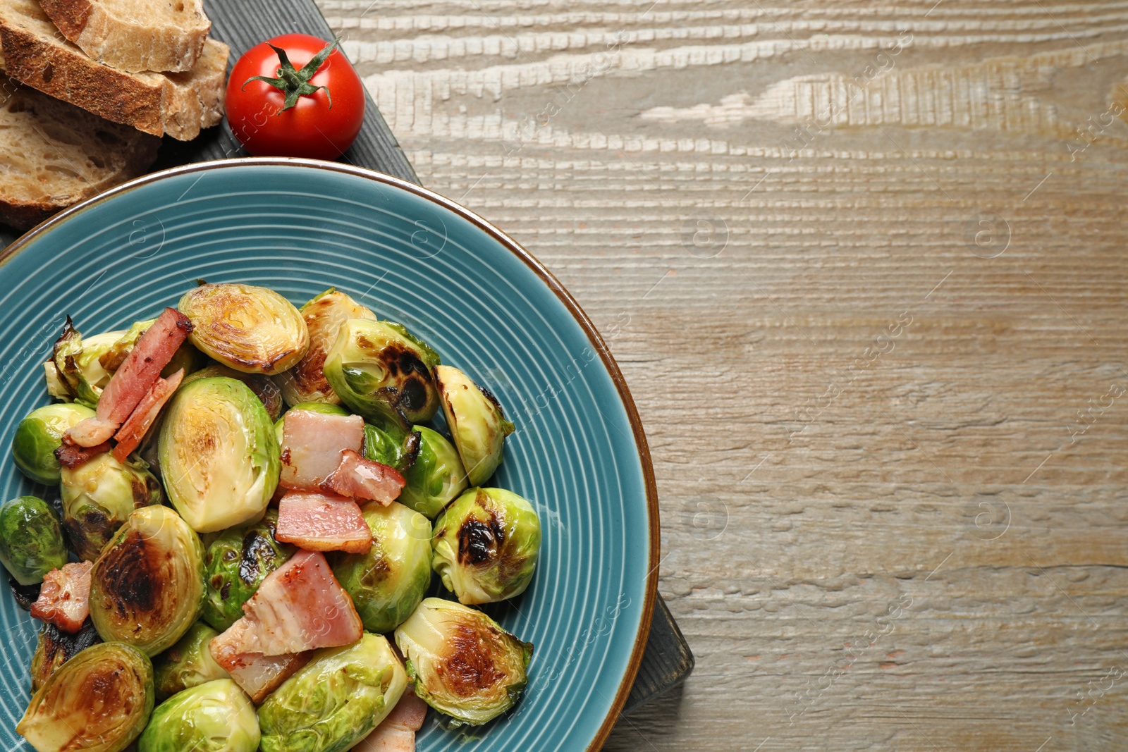 Photo of Delicious Brussels sprouts with bacon in plate on wooden table, flat lay. Space for text