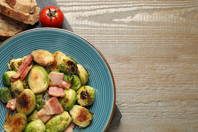 Delicious Brussels sprouts with bacon in plate on wooden table, flat lay. Space for text