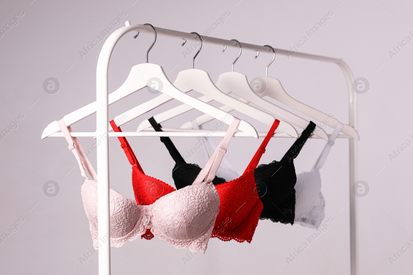 Photo of Hangers with beautiful lace bras on rack against grey background. Stylish underwear