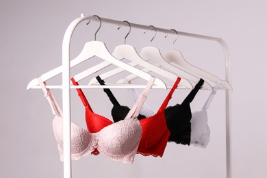 Hangers with beautiful lace bras on rack against grey background. Stylish underwear