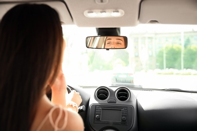 Photo of Young woman looking in rearview mirror of car
