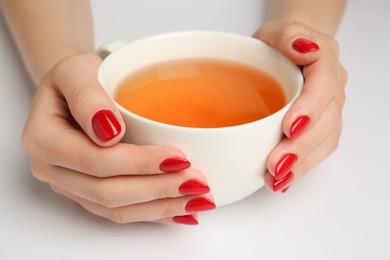 Photo of Woman with red polish on nails holding cup of hot drink on white background, closeup