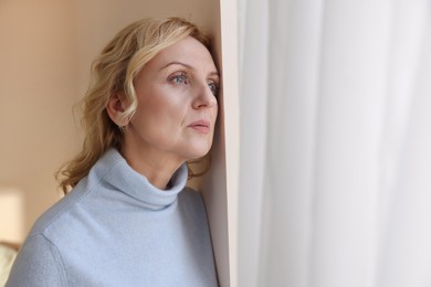 Photo of Upset middle aged woman near window at home. Loneliness concept