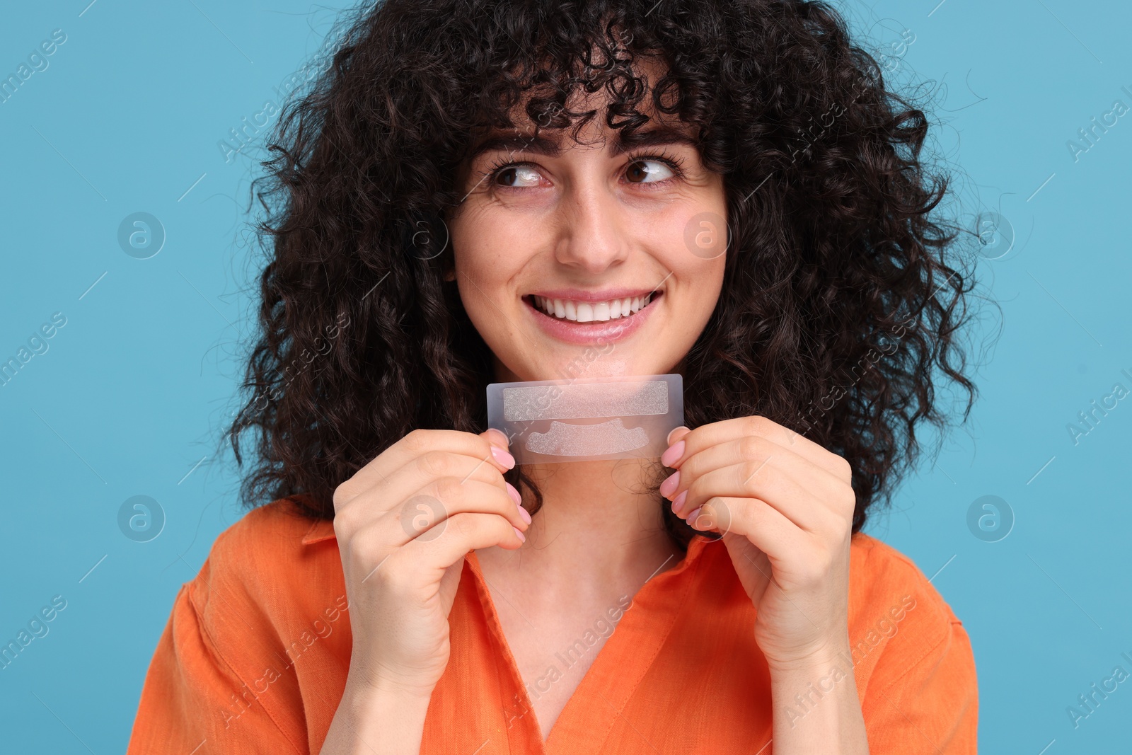 Photo of Young woman holding teeth whitening strips on light blue background