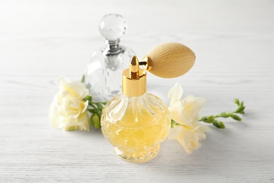 Photo of Different perfume bottles and flowers on white wooden background