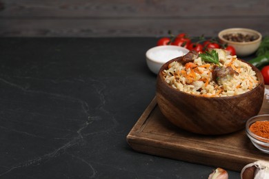 Photo of Delicious pilaf in bowl and products on black textured table. Space for text
