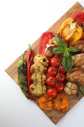 Photo of Wooden board with tasty grilled vegetables, meat, rosemary and basil isolated on white, top view