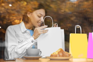 Special Promotion. Happy young woman looking into shopping bag in cafe, view from outdoors