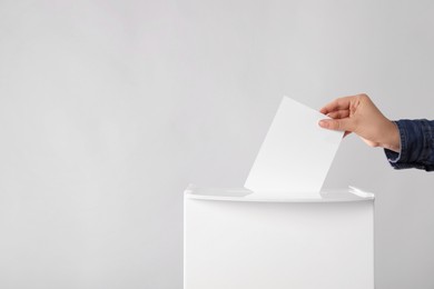 Woman putting her vote into ballot box on light grey background, closeup. Space for text