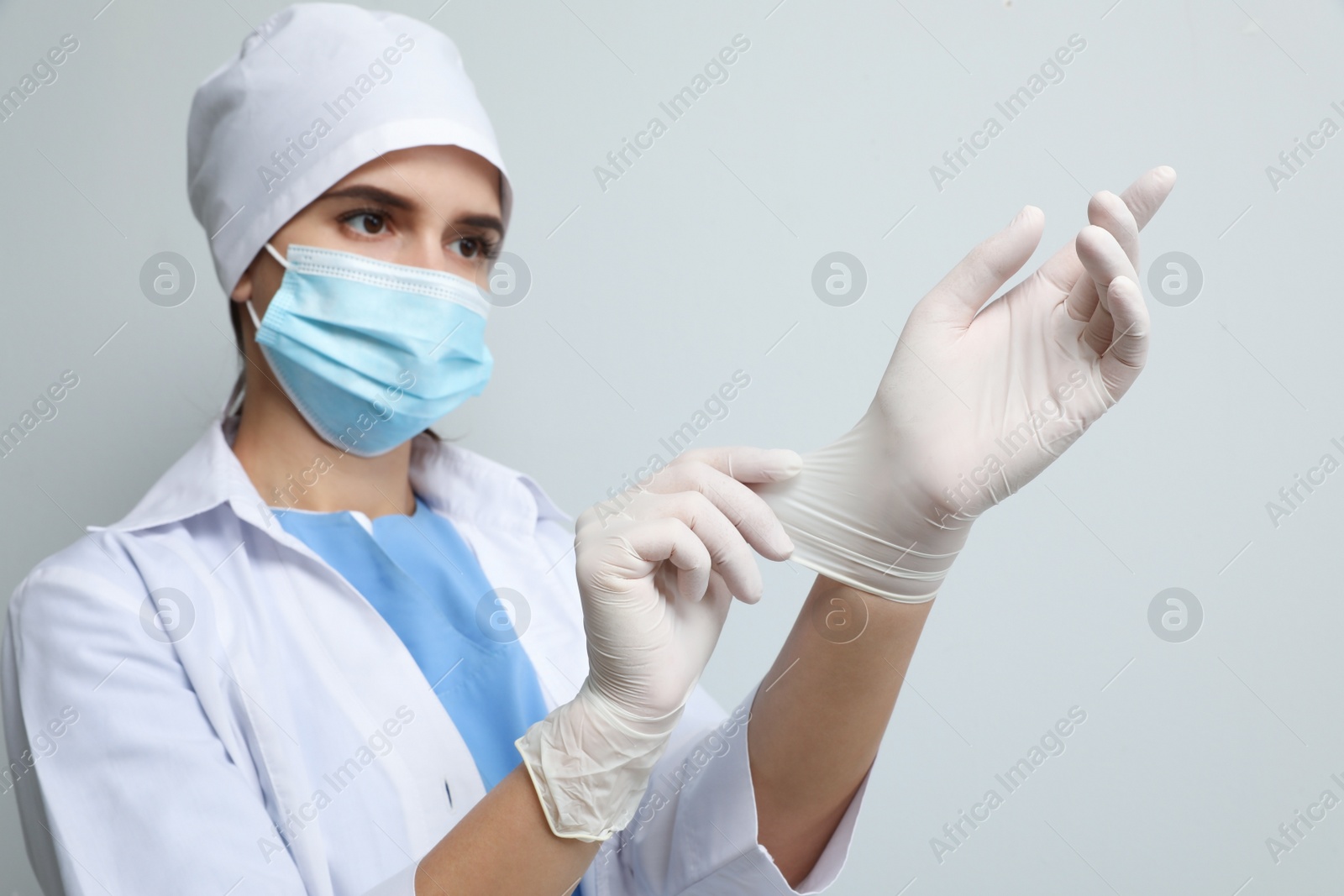 Photo of Doctor in protective mask putting on medical gloves against light grey background