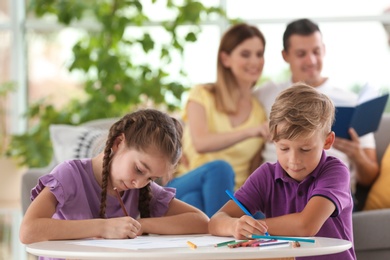 Photo of Children drawing at table near parents indoors. Happy family