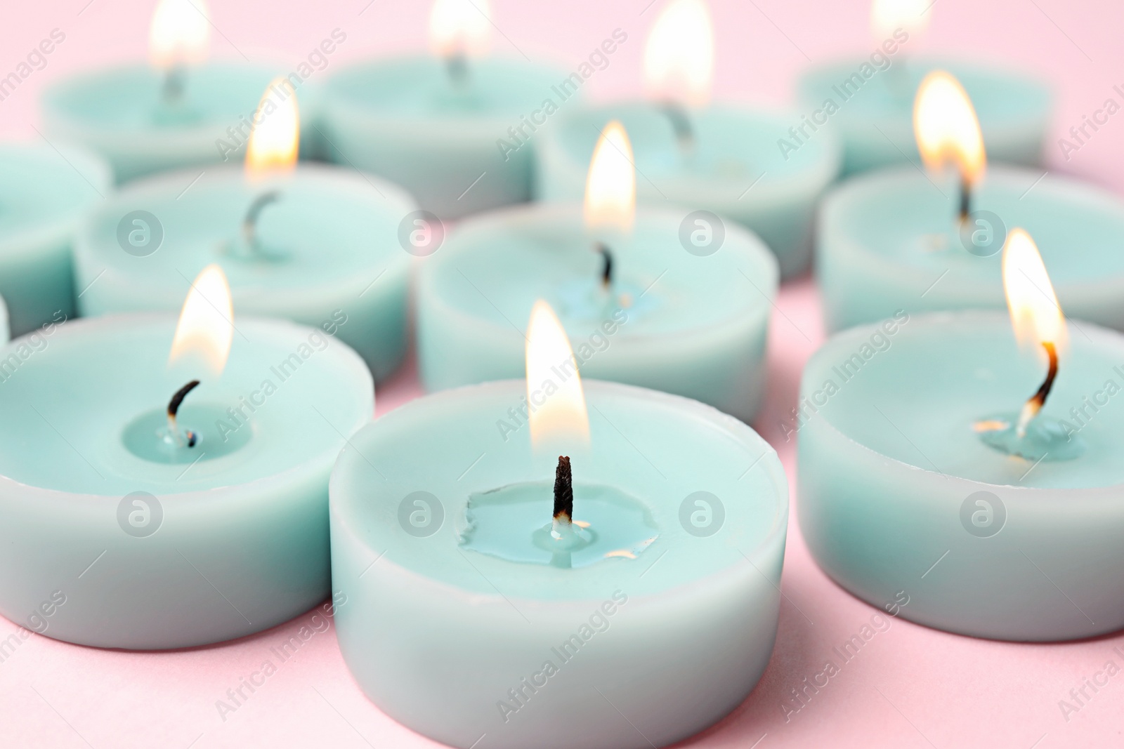 Photo of Burning light blue decorative candles on pink background