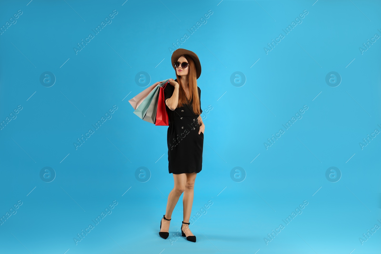 Photo of Beautiful young woman with paper shopping bags on light blue background